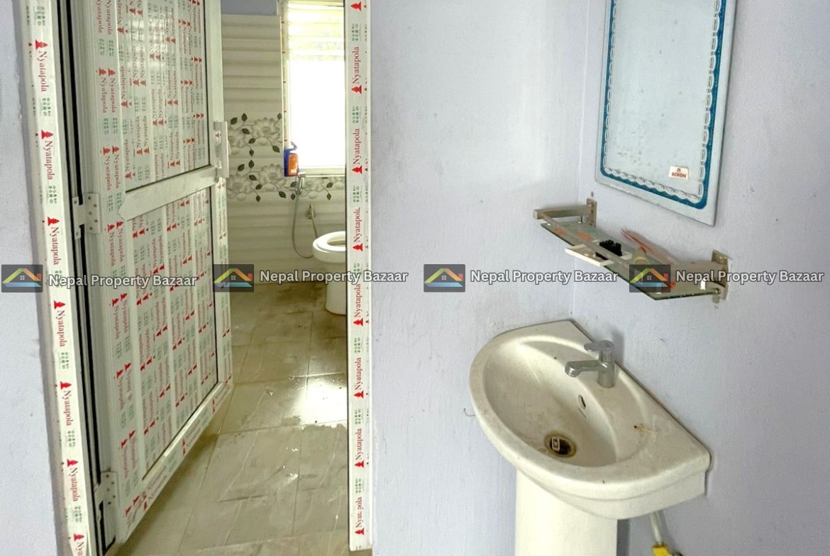 Partially finished bathroom with a pedestal sink, wall mirror, and blue walls; doorway wrapped in protective tape; toilet visible beyond.