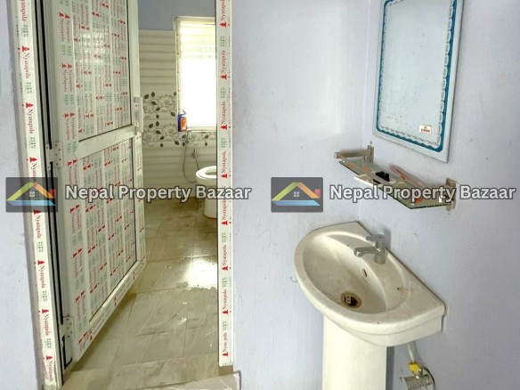 Partially finished bathroom with a pedestal sink, wall mirror, and blue walls; doorway wrapped in protective tape; toilet visible beyond.