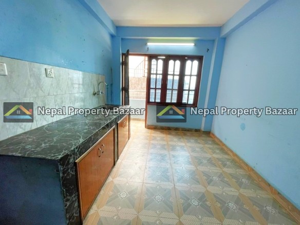 Blue kitchen with marble countertop and wooden cabinet doors, a sink on the left, and a doorway to a balcony through a grid-window door edge. When needed, natural light fills the room.