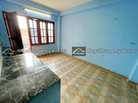 Small blue kitchen room with a dark cabinet by a large window, and a green marble countertop along the left wall, tiled floor.