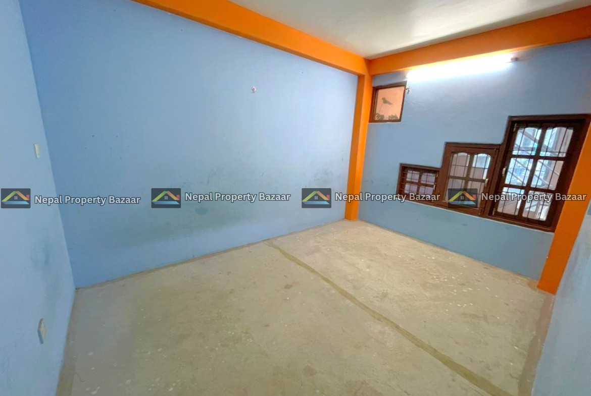 Small empty blue-walled room with orange trim and exposed concrete floor; brown-framed windows with bars along one wall.