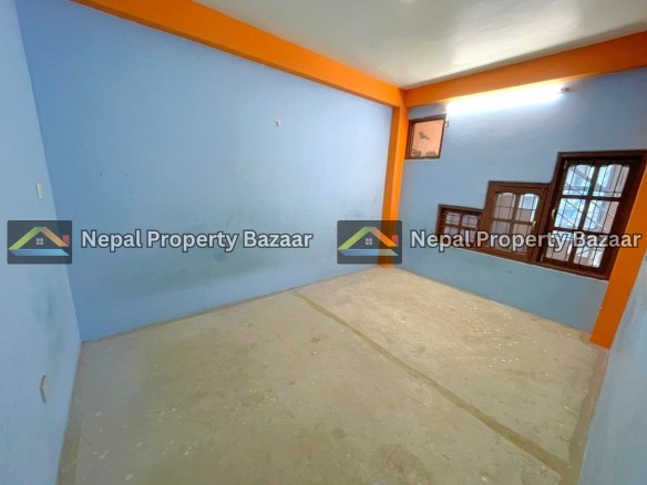 Small empty blue-walled room with orange trim and exposed concrete floor; brown-framed windows with bars along one wall.