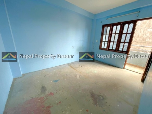 Empty blue-painted room with a concrete floor and paint splatters, featuring large wooden-framed windows that open to a balcony.