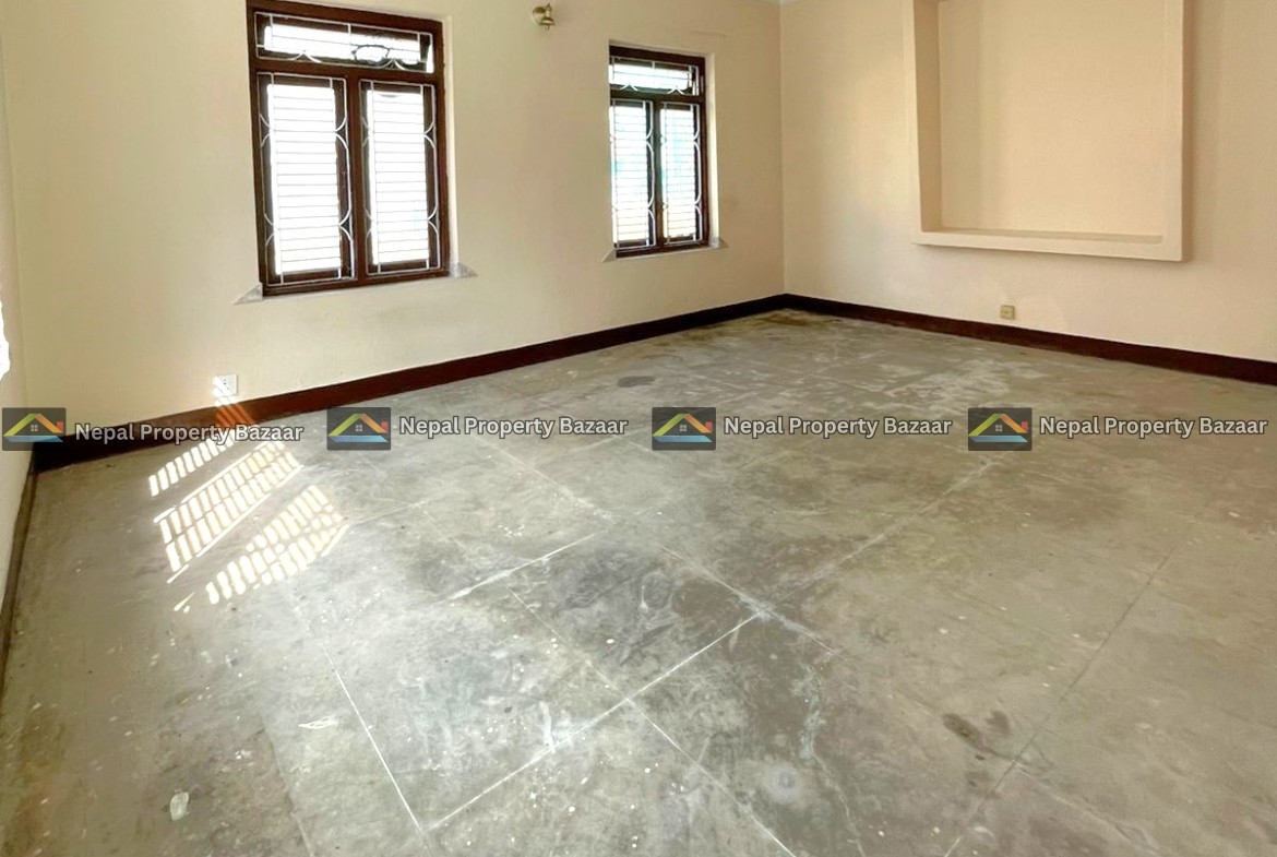 Empty living room with two wooden-framed windows, beige walls, and a square recessed niche on one wall; concrete floor and natural light.