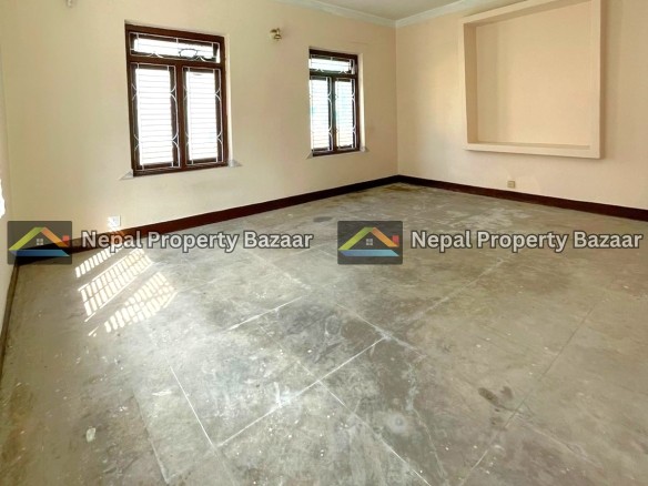 Empty living room with two wooden-framed windows, beige walls, and a square recessed niche on one wall; concrete floor and natural light.