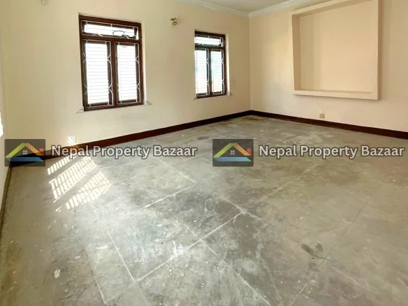 Empty living room with two wooden-framed windows, beige walls, and a square recessed niche on one wall; concrete floor and natural light.