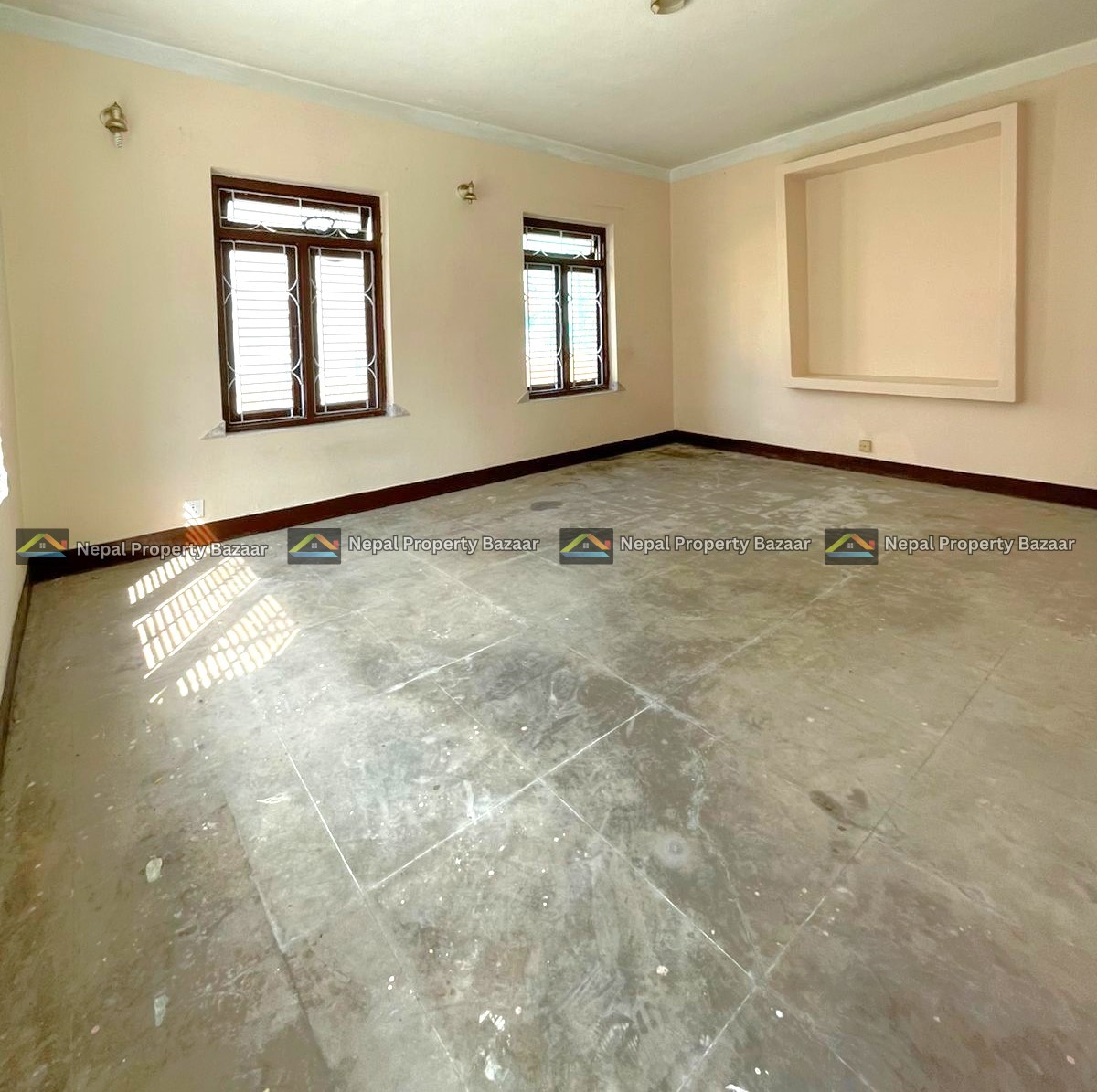 Empty living room with two wooden-framed windows, beige walls, and a square recessed niche on one wall; concrete floor and natural light.