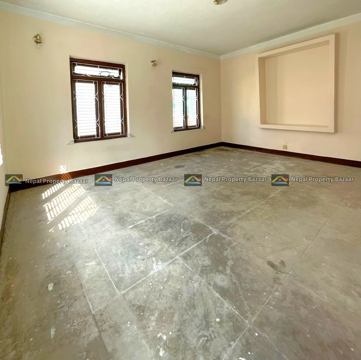 WhatsApp Image 2026-04-19 at 14.17.57 (1) Empty living room with two wooden-framed windows, beige walls, and a square recessed niche on one wall; concrete floor and natural light.