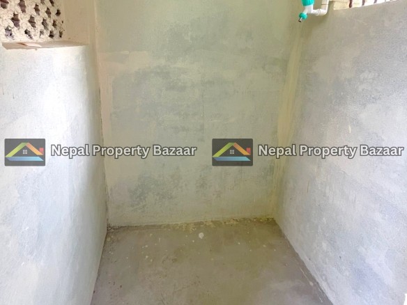 Small unfinished shower area with rough concrete walls, a green-handled faucet on the right, and a barred window near the top right.
