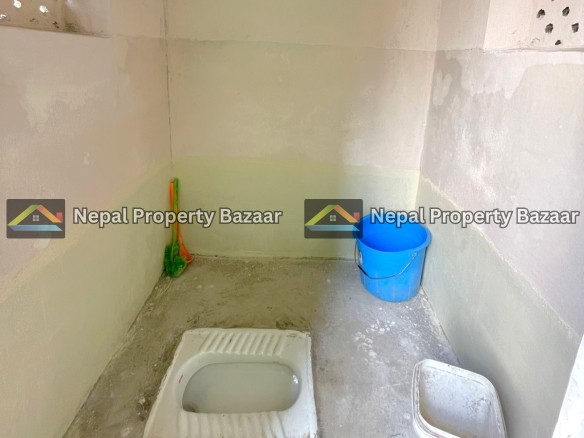 A squat toilet in a bare concrete bathroom; a blue bucket and a white plastic container sit on the floor nearby.